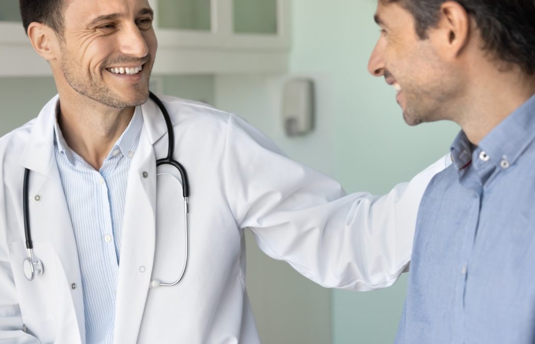 Cheerful supportive empathetic doctor man touching shoulder of patient on appointment in hospital office, congratulating on successful treatment result, rehabilitation, good checkup