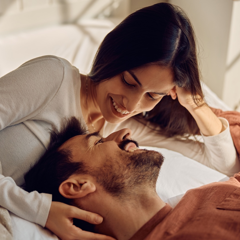 Happy couple in love communicating face to face while relaxing on a bed.