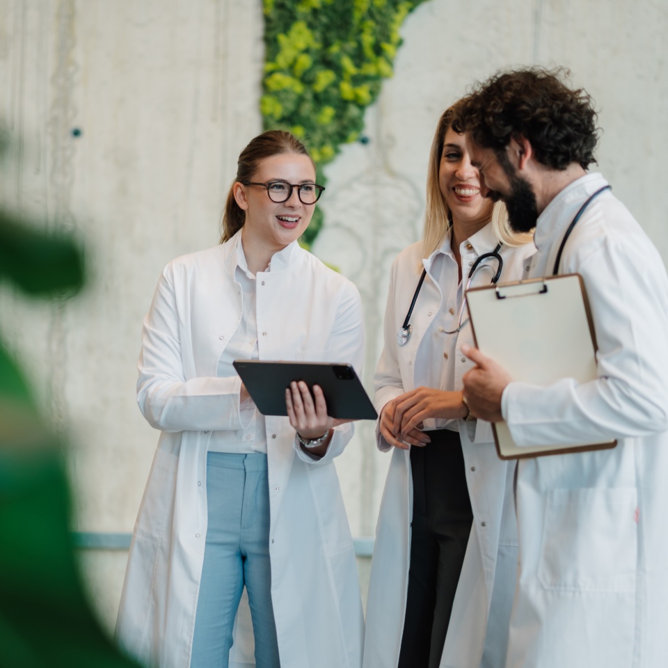 Doctors using digital tablet and discussing patient information, working together in modern hospital corridor with plants