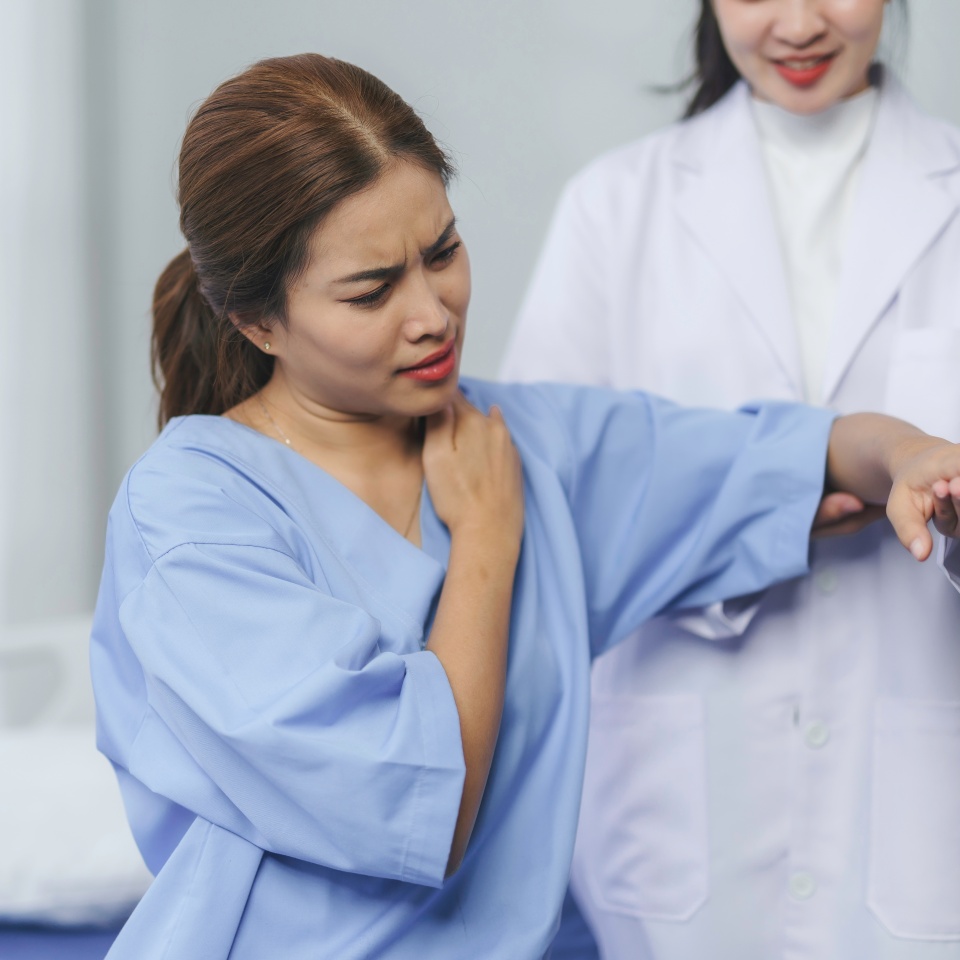 Doctor examining a patient's shoulder in a hospital room, assessing for shoulder and neck pain while providing professional care and support