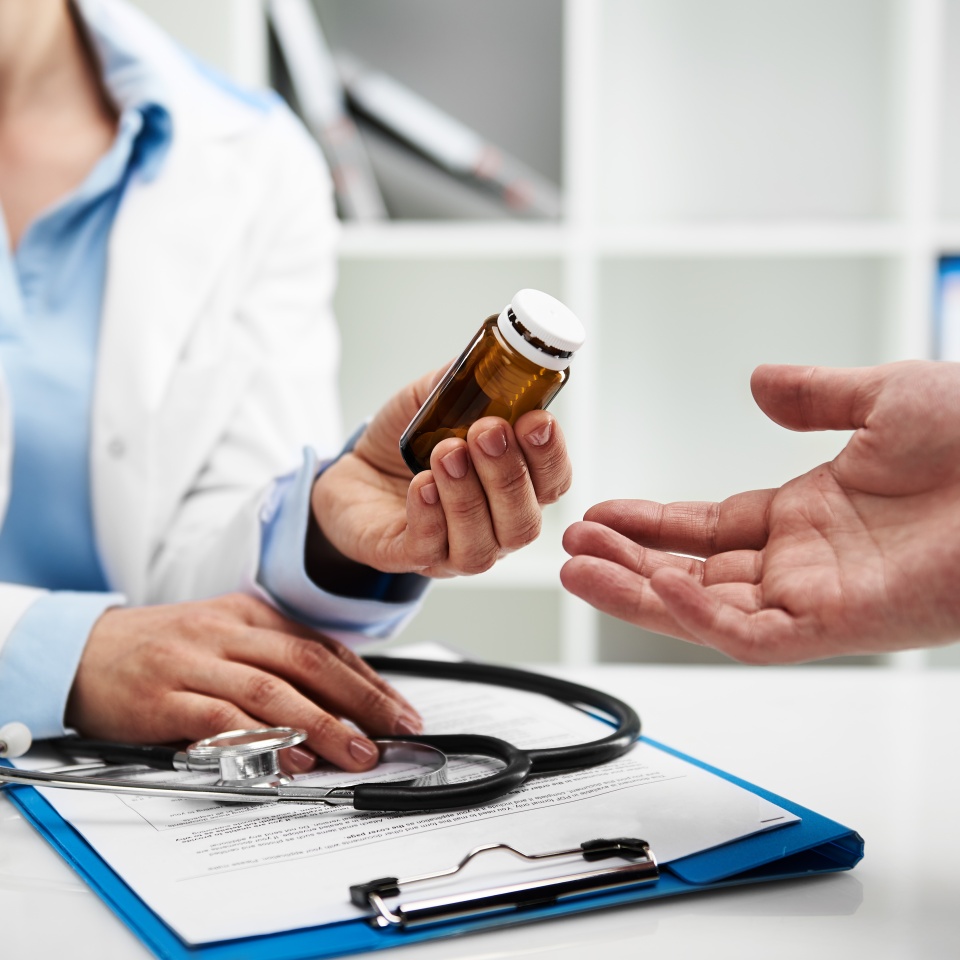 Female doctor giving pills bottle to male patient in clinic. Concept of healthcare, medical treatment and insurance.