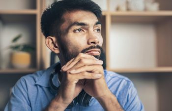 Thoughtful young bearded man sad looking out window while sitting on desk at home office
