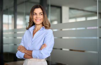 Happy confident mature professional business woman standing at work in office arms crossed looking away, proud hispanic middle aged businesswoman leader executive thinking of future success.