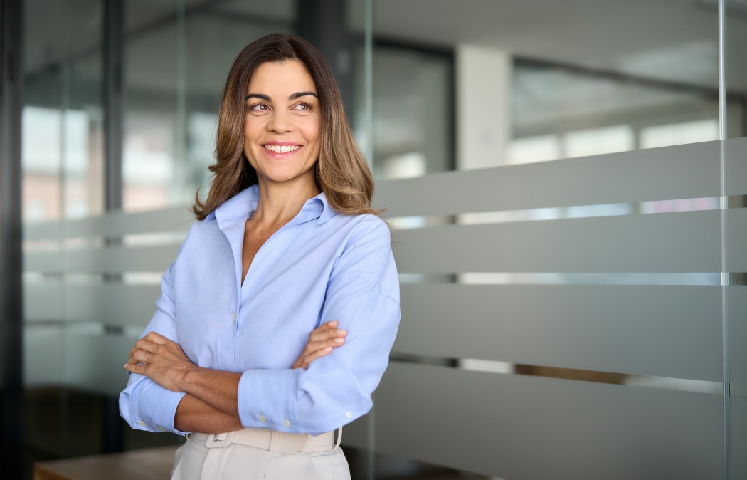 Happy confident mature professional business woman standing at work in office arms crossed looking away, proud hispanic middle aged businesswoman leader executive thinking of future success.