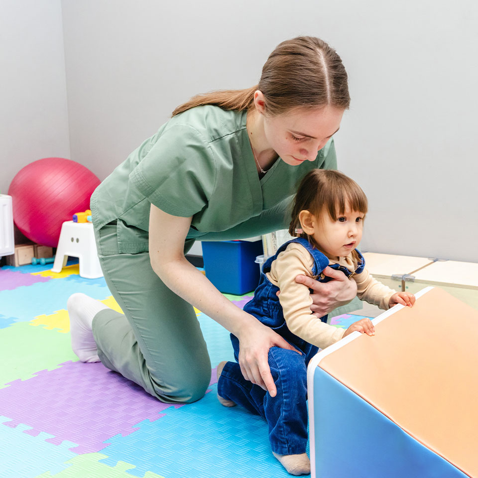 Physiotherapist assisting young child with coordination exercise in rehab center