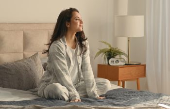 Caucasian brunette woman sitting on bed bedroom home touching neck massage good morning calm comfortable cozy inside awake healthcare in pajamas relaxing smiling wellbeing peaceful apartment recovery