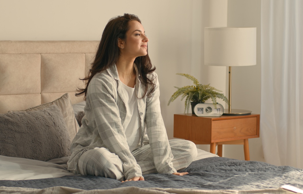 Caucasian brunette woman sitting on bed bedroom home touching neck massage good morning calm comfortable cozy inside awake healthcare in pajamas relaxing smiling wellbeing peaceful apartment recovery
