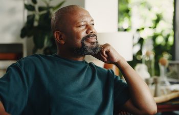 Relax, smile and reflection with mature black man in home for nostalgia, vision or positive mindset. Thinking, daydreaming and happy person with peace, calm and thoughts in living room on weekend.